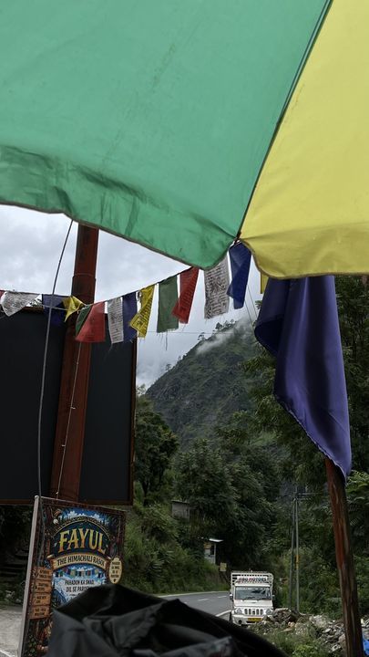 Prayer flags hanging under a green and yellow umbrella by the road