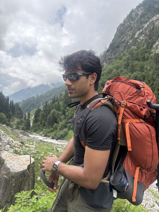 A trekker with an orange pack above a river valley
