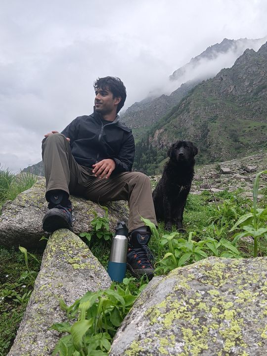 A trekker on a lichen-covered rock beside a black dog