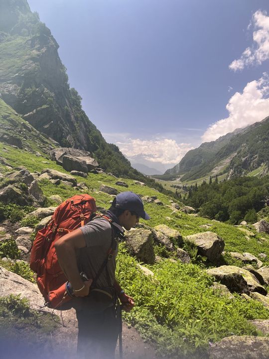 A trekker with an orange pack looking down a sunlit valley