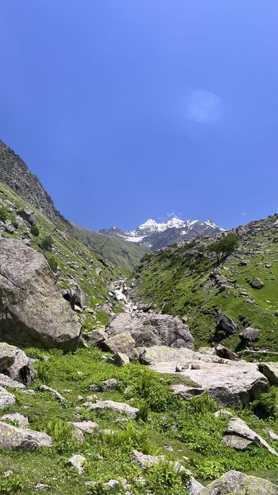 A stony stream bed leading up to a snow peak under blue sky