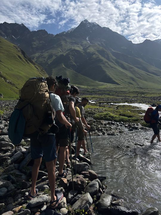 A line of trekkers with poles waiting to wade a stream