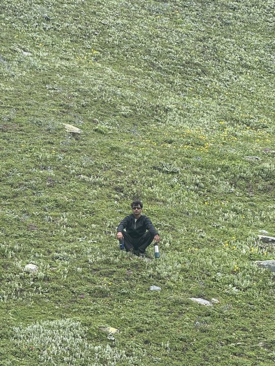 A trekker sitting alone in a wide green meadow