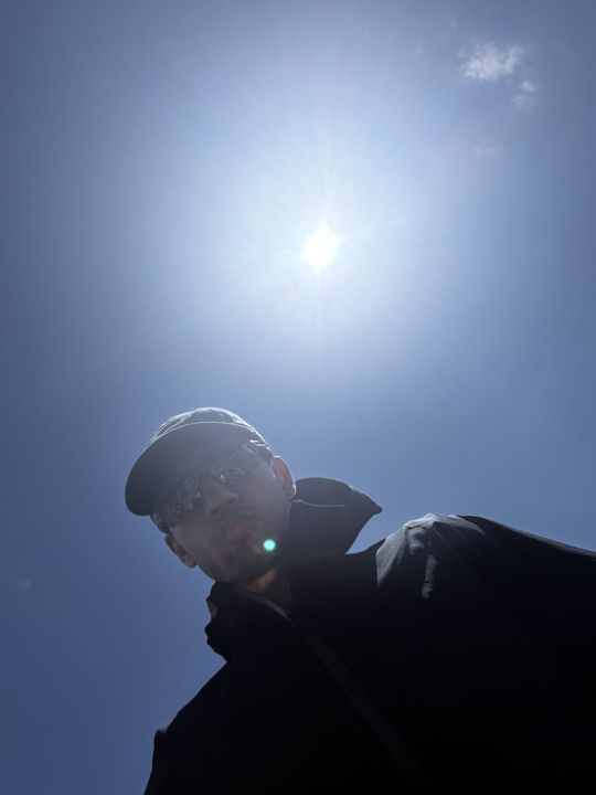 A trekker in a helmet looking down, the sun bright above