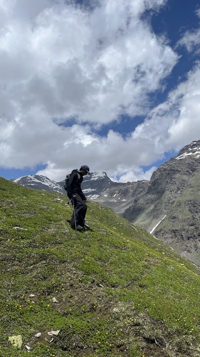 A lone trekker on a green slope as cloud clears from the peaks