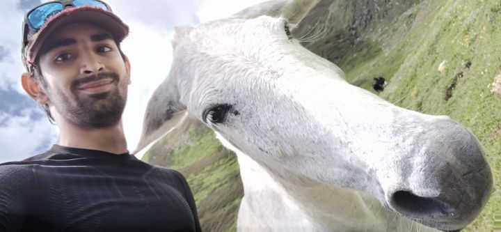 A selfie with a white horse leaning into the frame on a green slope