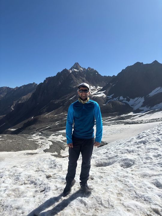 A trekker in a blue top standing on snow below jagged peaks